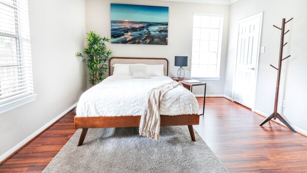 A bedroom with a wooden bed, a large window, a painting on the wall, and a coat rack. - COMFY COZY MED CENTER HOME (Houston)