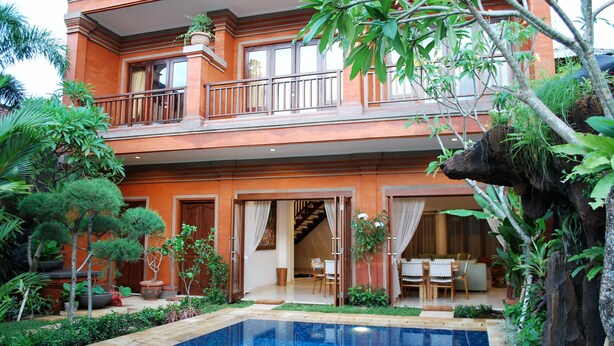 Um edifício de dois andares com piscina, rodeado por vegetação exuberante e plantas em vasos.