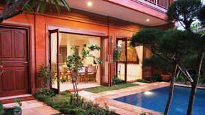 Área junto à piscina com espaço para refeições, uma porta de madeira e um pequeno jardim.