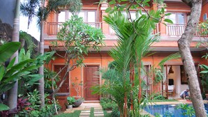 Um edifício de dois andares com piscina, rodeado por vegetação exuberante e palmeiras.