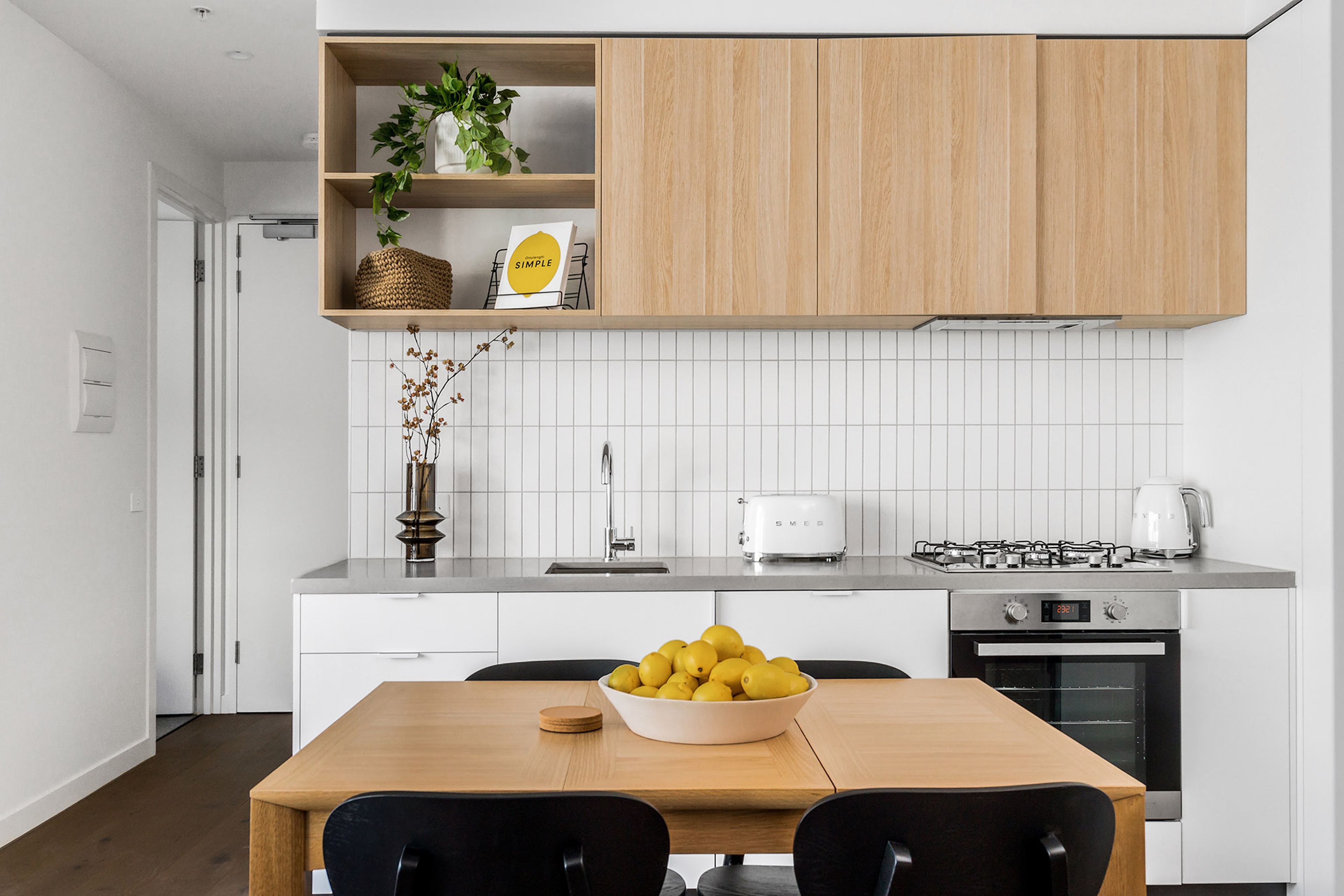 Una cocina moderna con armarios blancos, estufa de acero inoxidable y un comedor con mesa y sillas de madera.