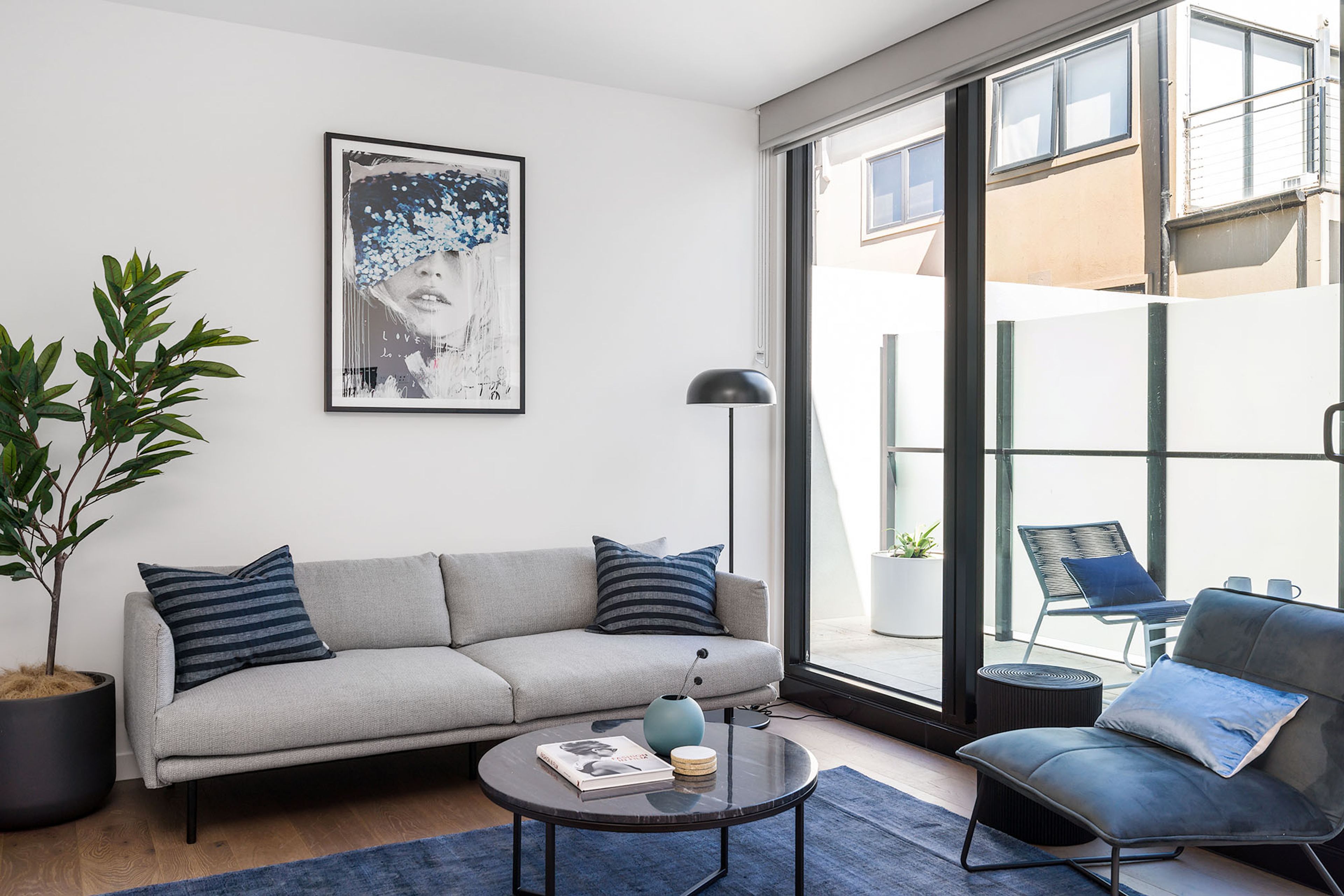 A modern living room with a grey sofa, a round coffee table, and a large window offering a view of the outside.
