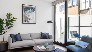 A modern living room with a grey sofa, a round coffee table, and a large window offering a view of the outside.