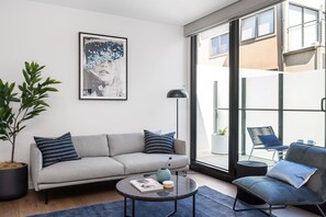 Una sala de estar moderna con un sofá gris, una mesa de centro redonda y un ventanal con vistas al exterior.