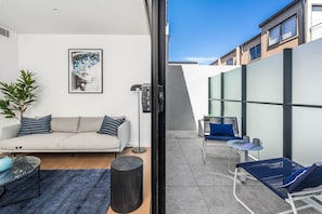 A modern living room with a sofa, a coffee table, and a floor lamp. - Axel Apartments 102 The Parkin (Glen Iris)