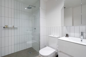 A modern bathroom with a glass-enclosed shower, a white toilet, and a sink with a mirror above it. - Axel Apartments 102 The Parkin (Glen Iris)