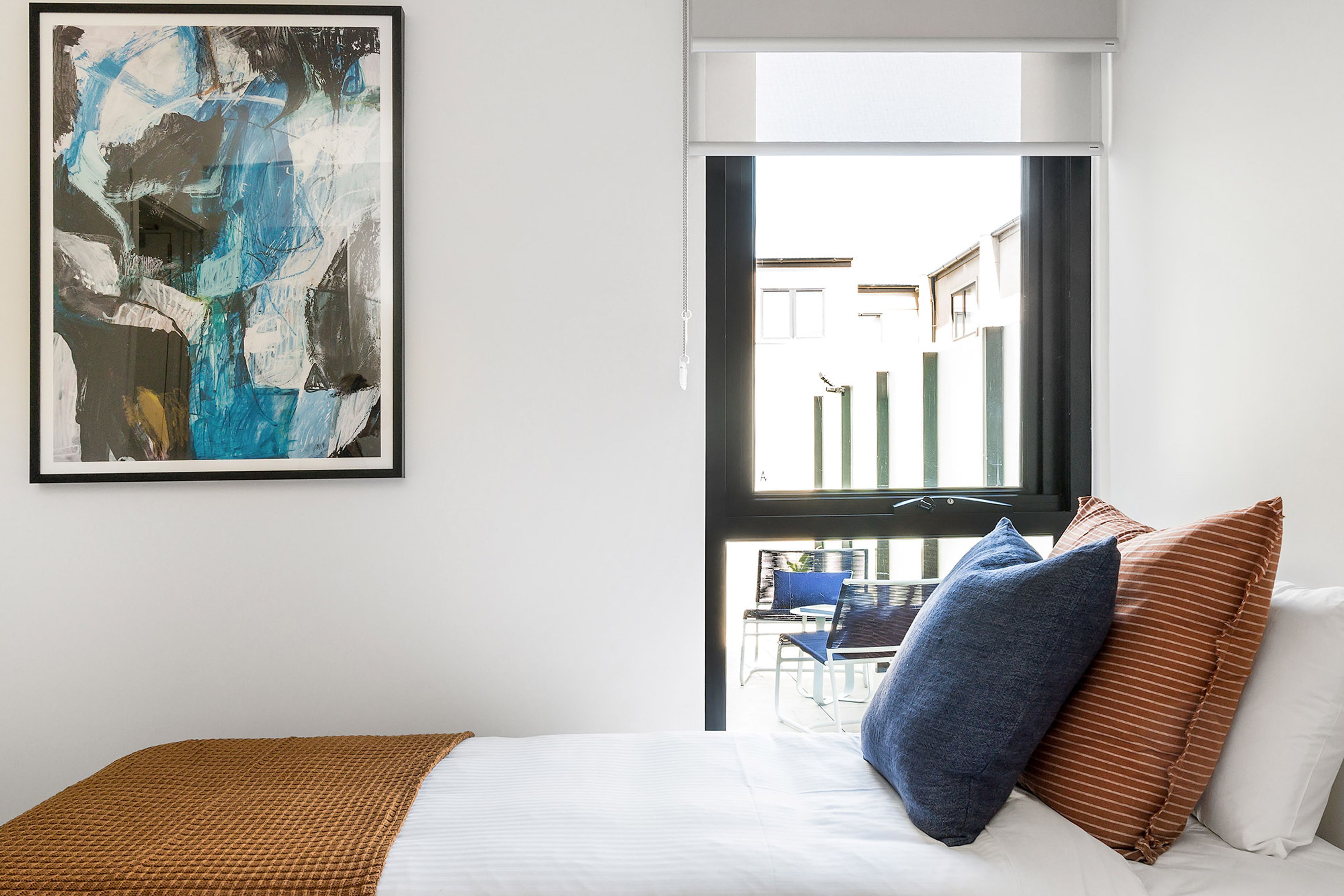 Une chambre d’hôtel avec une grande fenêtre, un lit avec une literie blanche et un oreiller bleu.