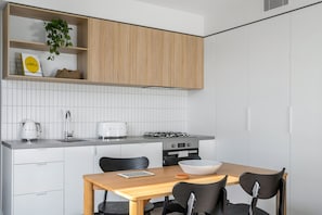 A modern kitchen with white cabinetry, a wooden dining table, and a gas stove.