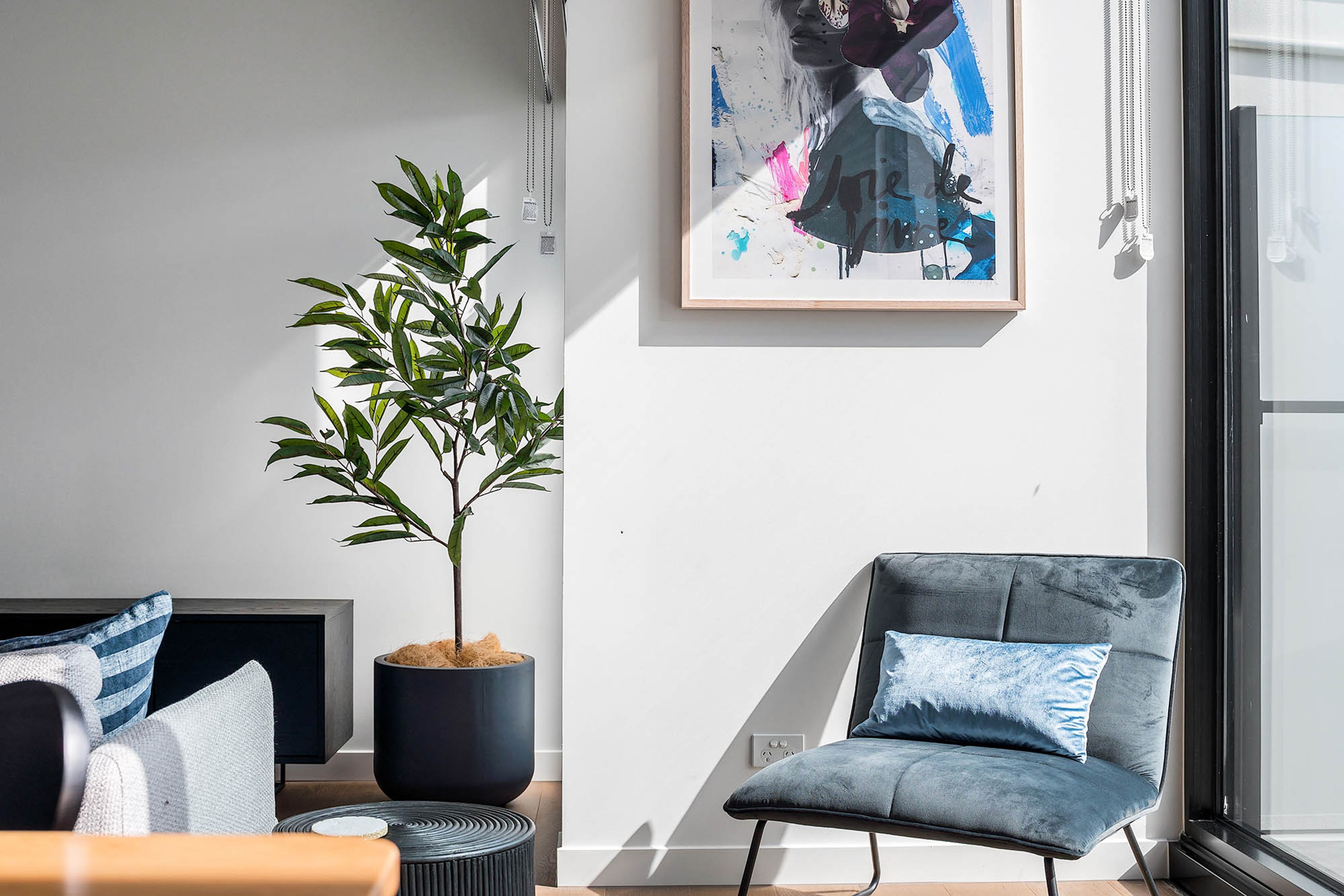 A modern living room with a sofa, a chair, a potted plant, and a framed abstract painting on the wall.