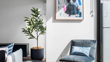 A modern living room with a sofa, a chair, a potted plant, and a framed abstract painting on the wall.