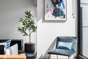 Una sala de estar moderna con un sofá, una silla, una planta en maceta y un cuadro abstracto enmarcado en la pared.