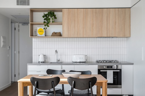 A modern kitchen with white cabinetry, a wooden dining table, and black chairs.