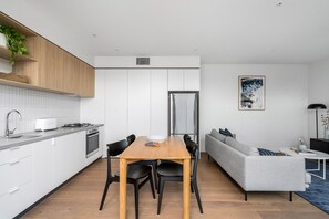 Una cocina moderna con armarios blancos, una mesa de comedor con sillas, un horno empotrado y una estufa a gas.