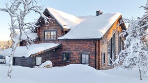En hytte med et stejlt tag og store vinduer, omgivet af sneklædte træer.