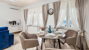A dining area with a round table set for four, beige chairs, and a view of the sea through large windows with sheer curtains. - Gorgeous apartment in Rijeka with WiFi (Rijeka)