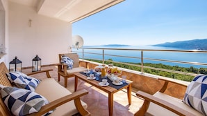 A balcony with a table set for tea, a sofa, and a view of a lake and mountains. - Gorgeous apartment in Rijeka with WiFi (Rijeka)