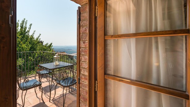 An open balcony with a table and chairs, a lantern, and a view of the landscape.