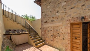 A stone building with a wooden door, a staircase, and a tiled patio area.