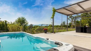 A swimming pool with a hot tub, surrounded by a covered patio area with seating and potted plants. - Stunning home in Malinska with heated swimming pool (Malinska)
