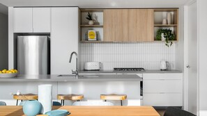 Eine moderne Küche mit einem Edelstahlkühlschrank, einem Toaster und einer Spüle. Es gibt Holzschränke und eine weiße Küchenrückwand.