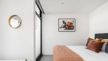 A bedroom with a bed, a bedside table, a mirror, a framed picture, and a window.