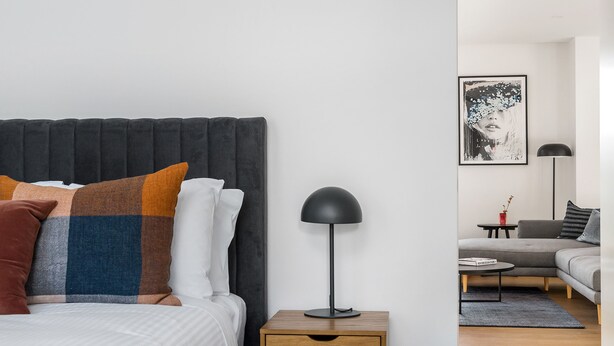 Et moderne soveværelse med en stor seng, sengeborde, en lampe ved siden af sengen og et billede i ramme på væggen.