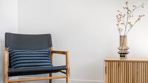 En træstol med mørk pude og et stribet pudebetræk, placeret ved siden af et træsidebord med en vase med tørrede grene.