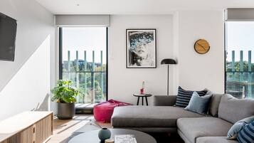 A modern living room with a grey sofa, a round coffee table, a potted plant, and a framed artwork on the wall.