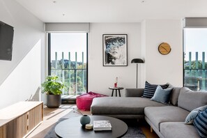 En moderne stue med en grå sofa, et rundt sofabord, en potteplante og et indrammet kunstværk på væggen.