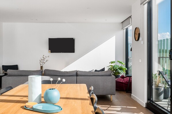 A modern living room with a grey sofa, a wooden dining table, and a large window.