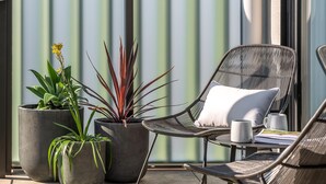 En terrasse med en fletstol, en potteplante og et bord med en kop og en bog.