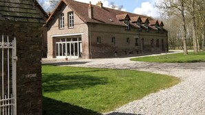A large brick building with a sloped roof, a covered entrance, and a gravel driveway. - CHARMING ALL COMFORT gîte near the Baie de Somme (Aigneville)
