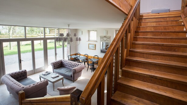 A spacious living area with a wooden staircase, large windows, and a dining set. - CHARMING ALL COMFORT gîte near the Baie de Somme (Aigneville)