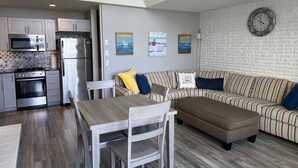 A modern kitchen with stainless steel appliances, a dining area with a wooden table and chairs, and a living room with a striped sofa and a clock on the wall. - Lakefront Condo on Crooked Lake, Convenient Location to Northern Michigan Cities (Conway)