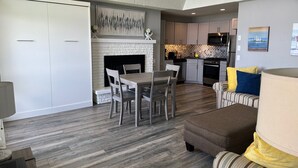 A modern kitchen with a fireplace, a dining area with a table and chairs, and a living area with a sofa and a lamp. - Lakefront Condo on Crooked Lake, Convenient Location to Northern Michigan Cities (Conway)