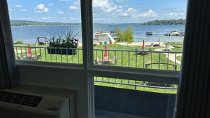 A room with a large window overlooking a lake, outdoor seating area, and a dock with boats. - Lakefront Condo on Crooked Lake, Convenient Location to Northern Michigan Cities (Conway)