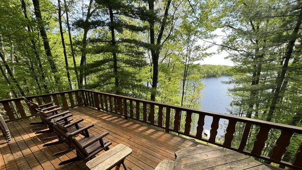 A wooden deck with benches and a table overlooking a lake surrounded by trees. - Lakefront Chalet - Badwater Lodge - Gorgeous Lake Views (Florence)