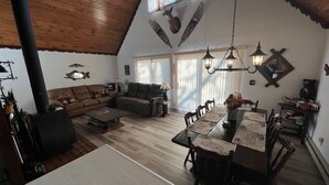 A cozy living room with a fireplace, a dining area with a long table, and a kitchen in the background. - Lakefront Chalet - Badwater Lodge - Gorgeous Lake Views (Florence)