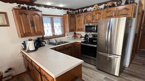 A kitchen with wooden cabinets, stainless steel appliances, a large island, and a window with blinds. - Lakefront Chalet - Badwater Lodge - Gorgeous Lake Views (Florence)