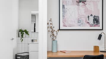 A modern interior with a desk, a framed abstract painting, a vase with dried flowers, and a trash bin.