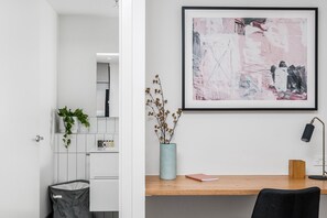 A modern interior with a desk, a framed abstract painting, a vase with dried flowers, and a trash bin. - Axel Apartments G02 The Faircroft (Glen Iris)