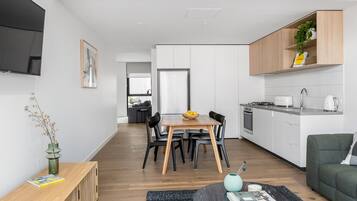 A modern kitchen with white cabinets, a dining area with a wooden table and chairs, and a living area with a green sofa.