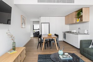 A modern kitchen with white cabinets, a dining area with a wooden table and chairs, and a living area with a green sofa.