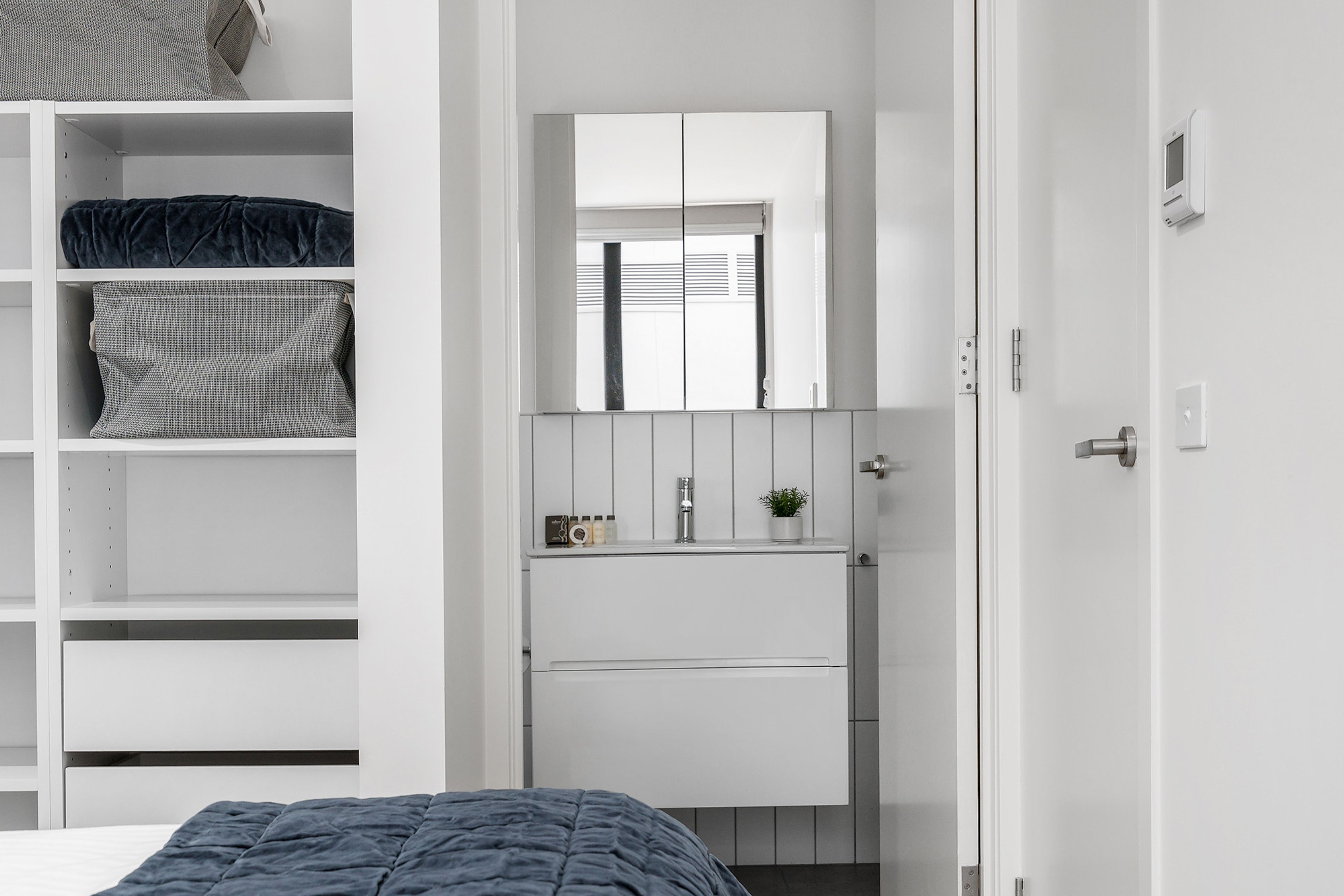 A bedroom with a bed, a wardrobe, a mirror, a sink, and a door.