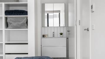 A bedroom with a bed, a wardrobe, a mirror, a sink, and a door.