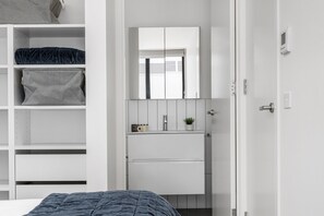 A bedroom with a bed, a wardrobe, a mirror, a sink, and a door.