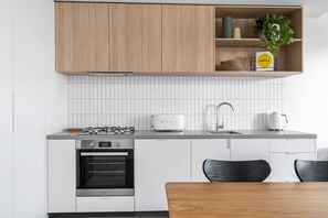 A modern kitchen with white cabinetry, a gas stove, an oven, a toaster, and a sink. - Axel Apartments G02 The Faircroft (Glen Iris)