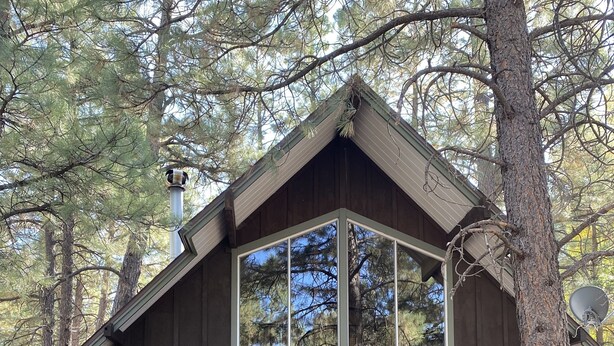 A cabin with a wooden deck, large windows, and a metal roof.