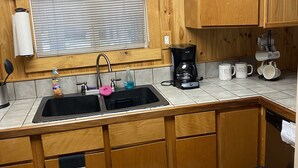 A kitchen with wooden cabinets, a black sink, a window with blinds, a coffee maker, and a towel rack.