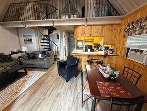 Una sala de estar moderna con un sofá, una mesa de comedor con sillas, una escalera y una zona de cocina.